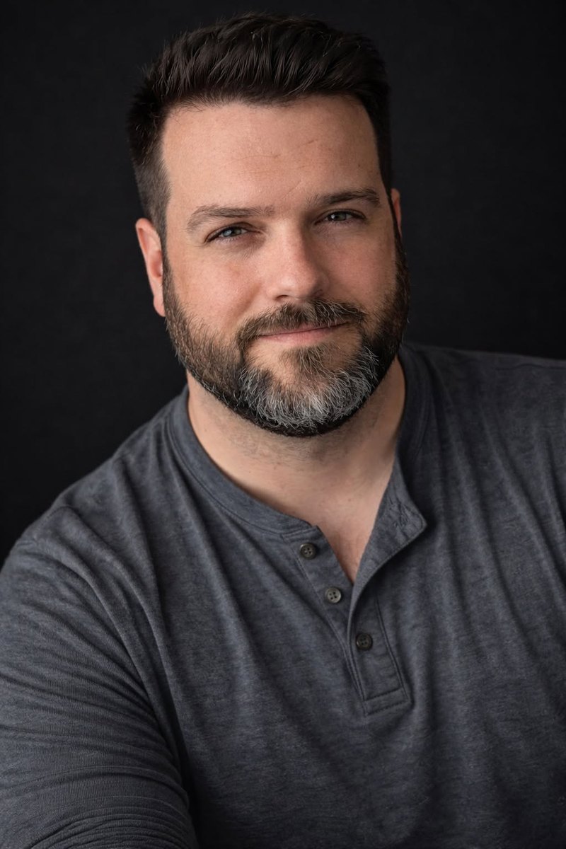 Portrait of Andrew Grupp, smiling slightly, with a salt-and-pepper beard and a gray henley shirt, against a dark background.